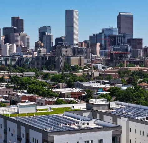 Why Selecting a Qualified Commercial Roofing Company is Crucial. View of Denver's downtown skyline with solar panels installed on rooftops, showcasing the city's blend of urban living and sustainable energy solutions.