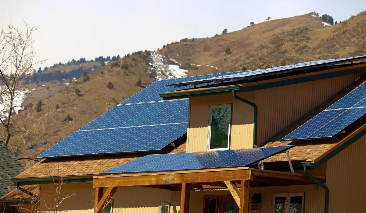 How Ice and Snow Buildup Can Impact Your Solar Panels. A modern home featuring solar panels on its roof, set against a backdrop of rolling hills and clear skies.