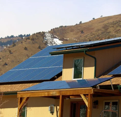 How Ice and Snow Buildup Can Impact Your Solar Panels. A modern home featuring solar panels on its roof, set against a backdrop of rolling hills and clear skies.