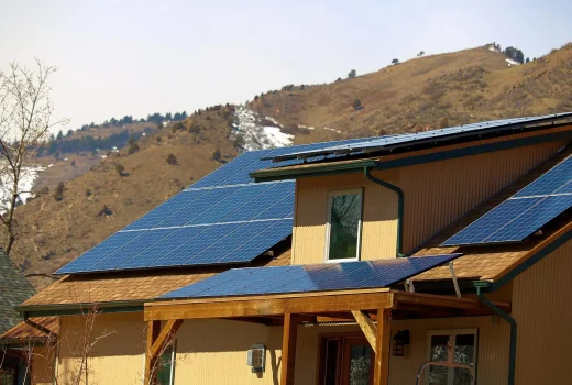 How Ice and Snow Buildup Can Impact Your Solar Panels. A modern home featuring solar panels on its roof, set against a backdrop of rolling hills and clear skies.