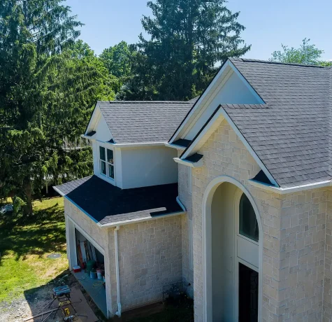 Why Are Insurance Companies Pulling Out of Some States? A beautiful two-story home showcasing a freshly installed gray shingle roof surrounded by lush greenery and trees.