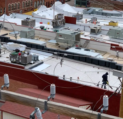 The Keys to Maintaining a Commercial Roof. Detailed view of a commercial rooftop with HVAC units, electrical wiring, and a worker conducting maintenance tasks.