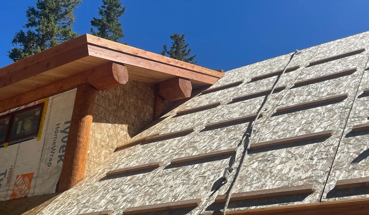 What's More Important Than a Roof Over Your Head? Close-up of a log-style roof under construction, featuring wooden beams and sheathing under a bright blue sky.