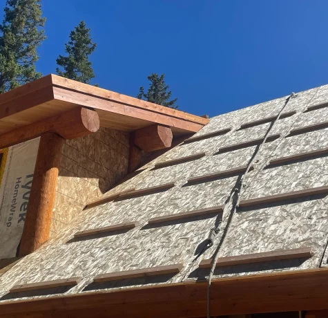 What's More Important Than a Roof Over Your Head? Close-up of a log-style roof under construction, featuring wooden beams and sheathing under a bright blue sky.