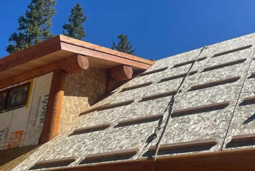 What's More Important Than a Roof Over Your Head? Close-up of a log-style roof under construction, featuring wooden beams and sheathing under a bright blue sky.