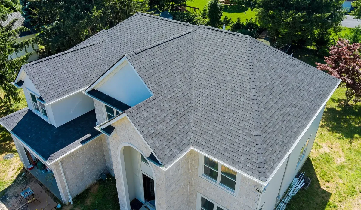 Roof Damage and How to Prevent It. A bird’s-eye view of a residential property with a newly installed gray roof, surrounded by trees and a landscaped yard.