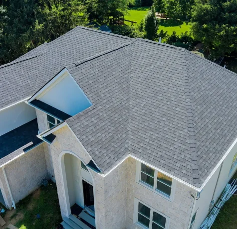 Roof Damage and How to Prevent It. A bird’s-eye view of a residential property with a newly installed gray roof, surrounded by trees and a landscaped yard.