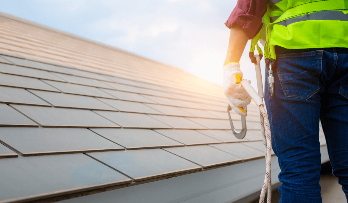 Roofer with safety harness inspecting residential shingle roof for certification