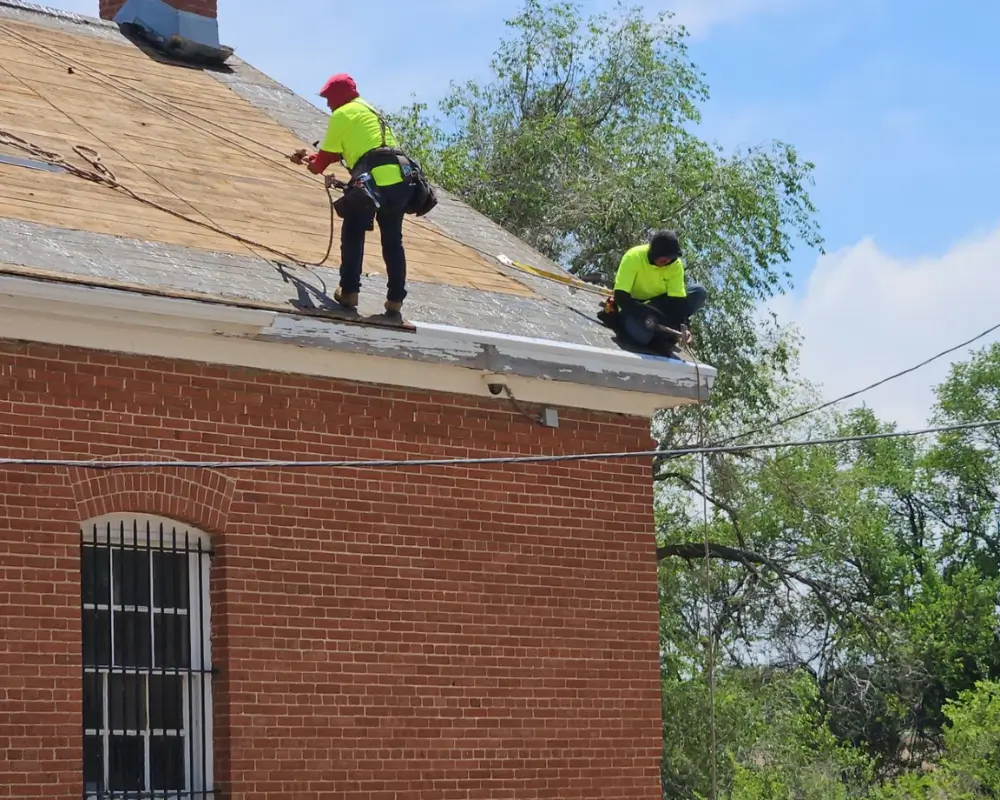 Two Premier roofers in safety gear working along the eave during the DHS Building 87 reroof