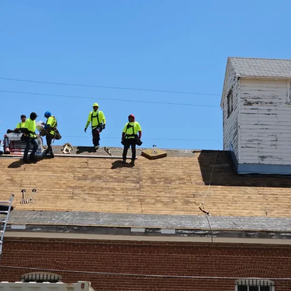 Premier roofing crew on the stripped deck of DHS Building 87 with new shingle bundles staged