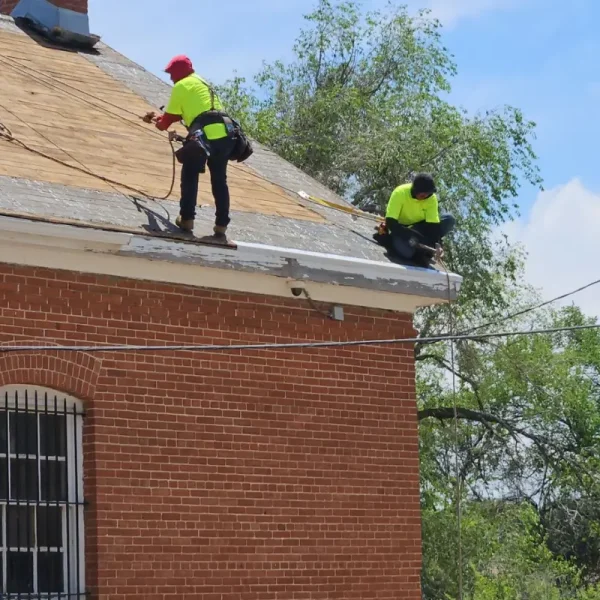 Two Premier roofers in safety gear working along the eave during the DHS Building 87 reroof